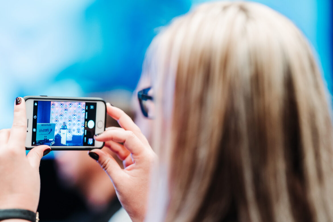 Conference attendee capturing speaker presentation on phone at Denver event